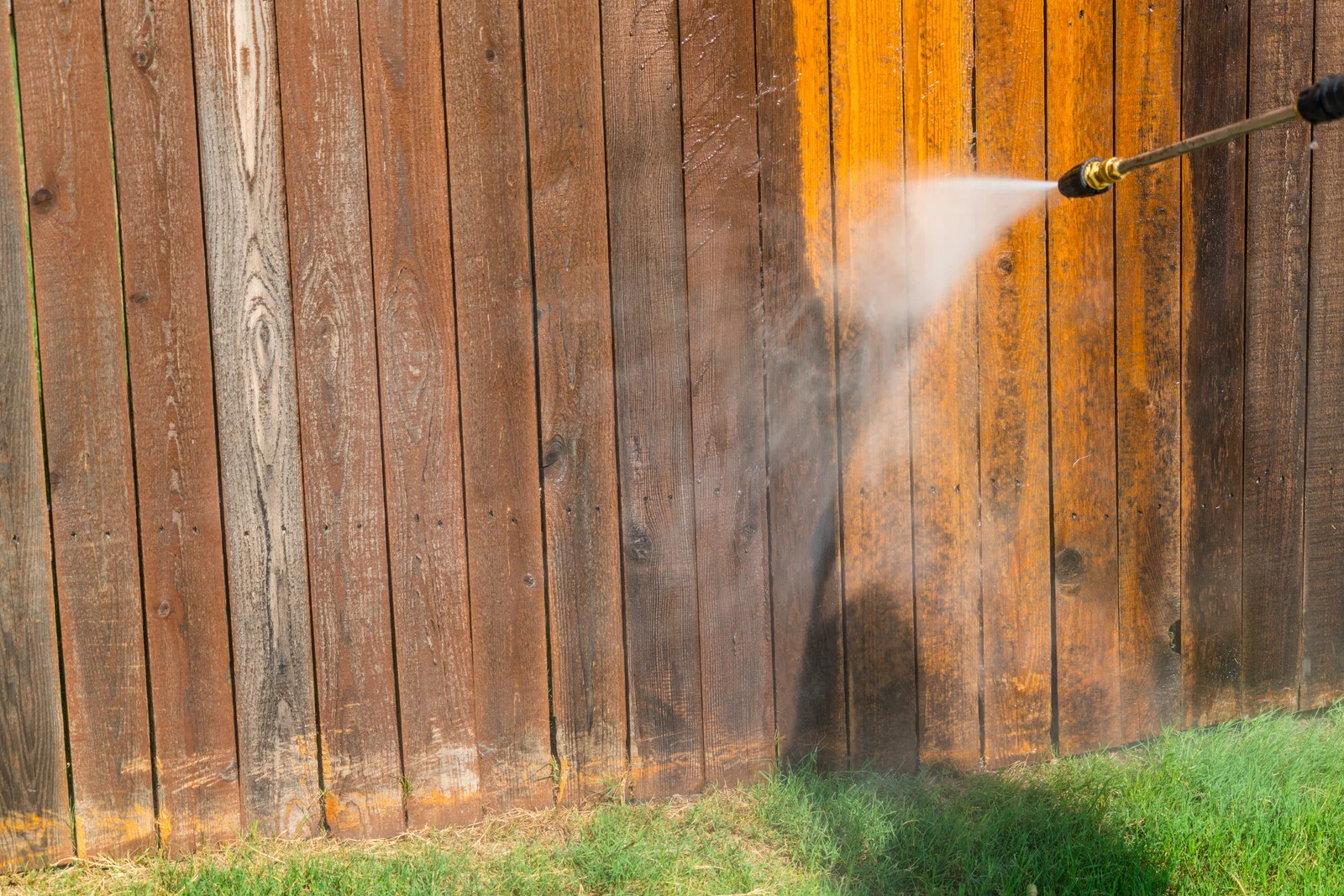 Pressure washing revealing clean wood on a weathered fence