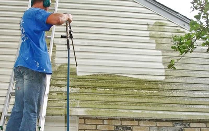Technician soft washing a home's vinyl siding