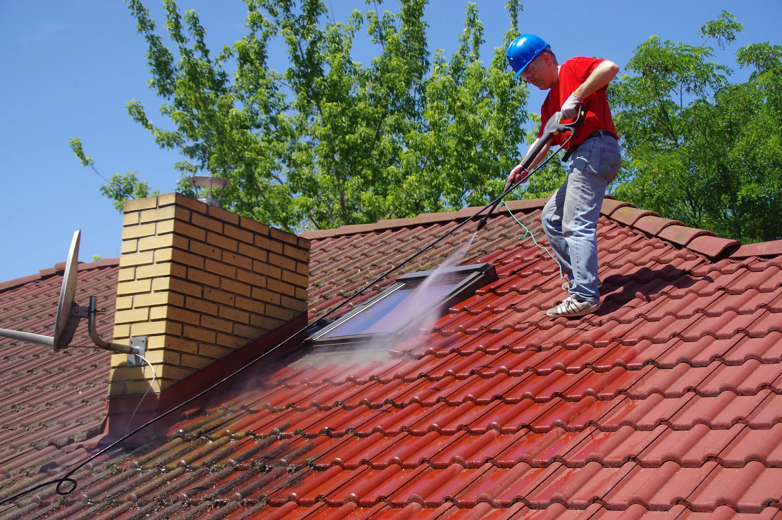 Technician cleaning a roof with low-pressure soft wash equipment